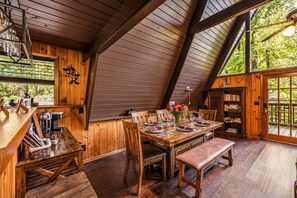 A dining area with a wooden table set for four, surrounded by chairs, in a room with wooden walls and a sloped ceiling. - Peaceful 4BR w/Hot Tub*Theater*Views*Resort Access (Gatlinburg)