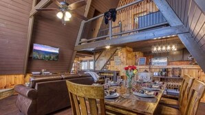 Un interior rústico con comedor, paredes de madera, una escalera y un televisor montado.