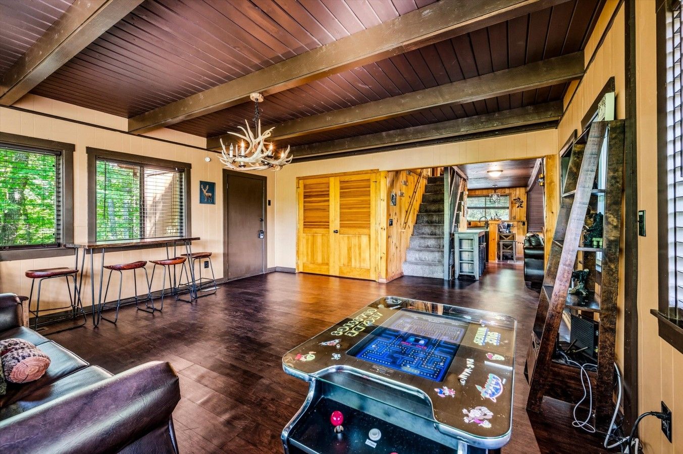 A spacious room with a wooden ceiling, a chandelier, a gaming table, and a staircase leading to another area.