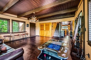 Ein geräumiger Raum mit Holzbalkendecke, einem Kronleuchter, einem Spieltisch und einer Treppe zu einem weiteren Bereich.