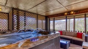 Un jacuzzi con revestimiento de madera, una terraza de madera y una zona de estar con cojines.