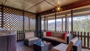 Un espacio al aire libre con techo, amueblado con mobiliario de mimbre, una mesa de centro de vidrio y vistas del paisaje circundante.