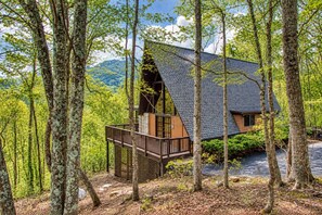 A cabin with a wooden deck and a steep roof, surrounded by a forested area. - Peaceful 4BR w/Hot Tub*Theater*Views*Resort Access (Gatlinburg)