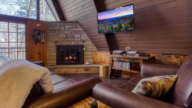 Un acogedor interior de cabaña con chimenea de piedra, sofás de cuero, televisor de pantalla plana y una estantería.