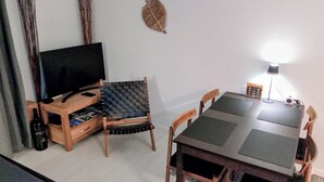 Ett kompakt vardagsrum med TV, en möbel i trä för förvaring och underhållning, ett matbord och stolar.