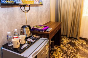 Habitación de hotel con minibar, una mesita con hervidor, una bandeja con botellas de agua, cafetera y control remoto.