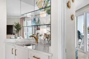 Eine moderne Küche mit Marmorarbeitsplatte, goldenen Griffen und einer Glasrückwand.