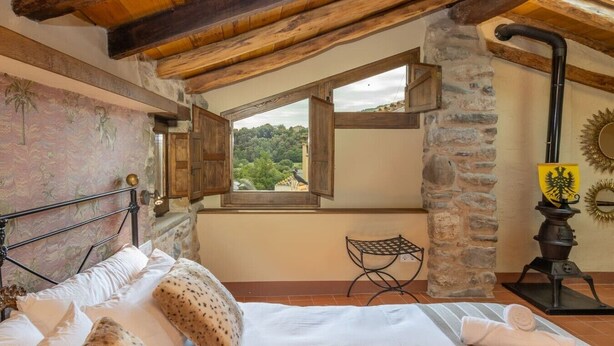 Een slaapkamer met een bed, een raam met uitzicht, een stenen zuil en een traditionele kachel.
