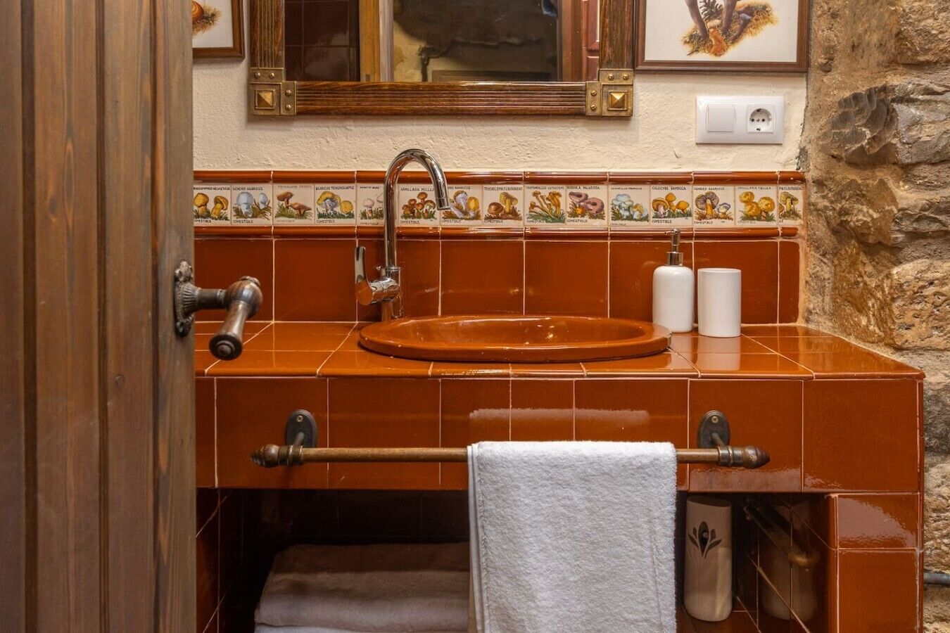 Um banheiro com pia em azulejo marrom, porta-toalhas, espelho e borda decorativa em azulejos.