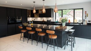 A modern kitchen with a central island, bar stools, pendant lighting, and a large window. - House Sleeps 10 With Enclosed Garden (Reading)