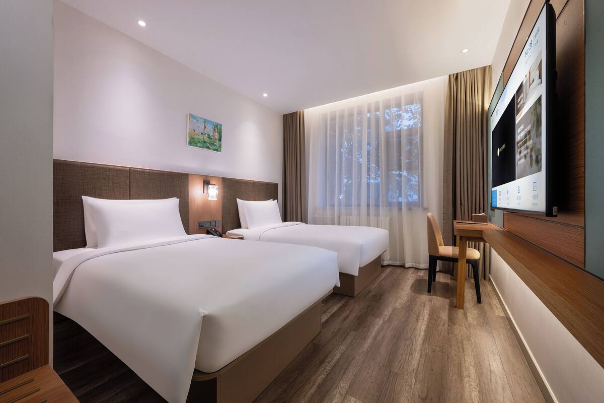 A hotel room with two beds, a desk, a chair, a TV, and a painting on the wall.