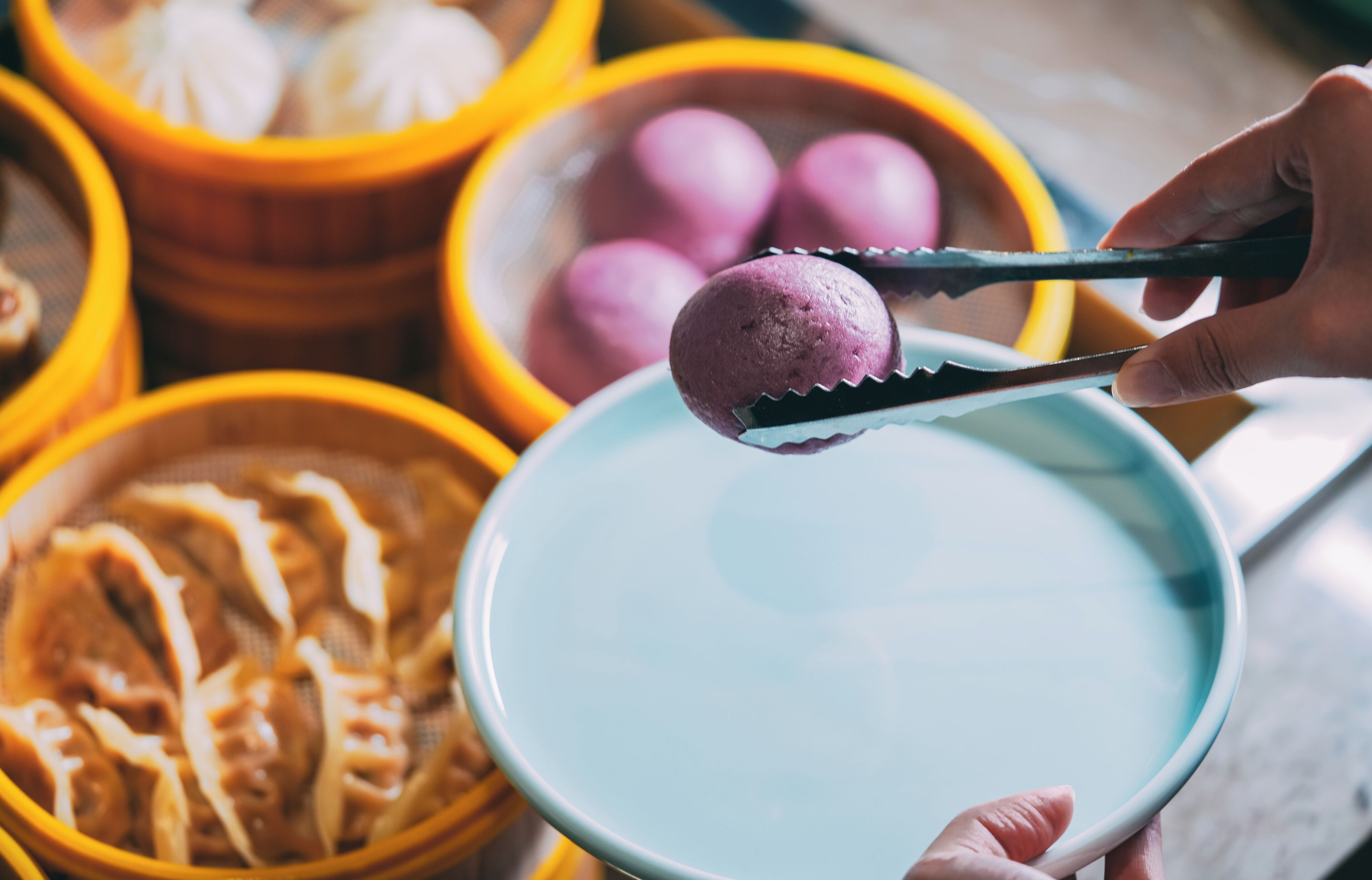 A hand holding a plate with a purple food item, surrounded by bowls of food.