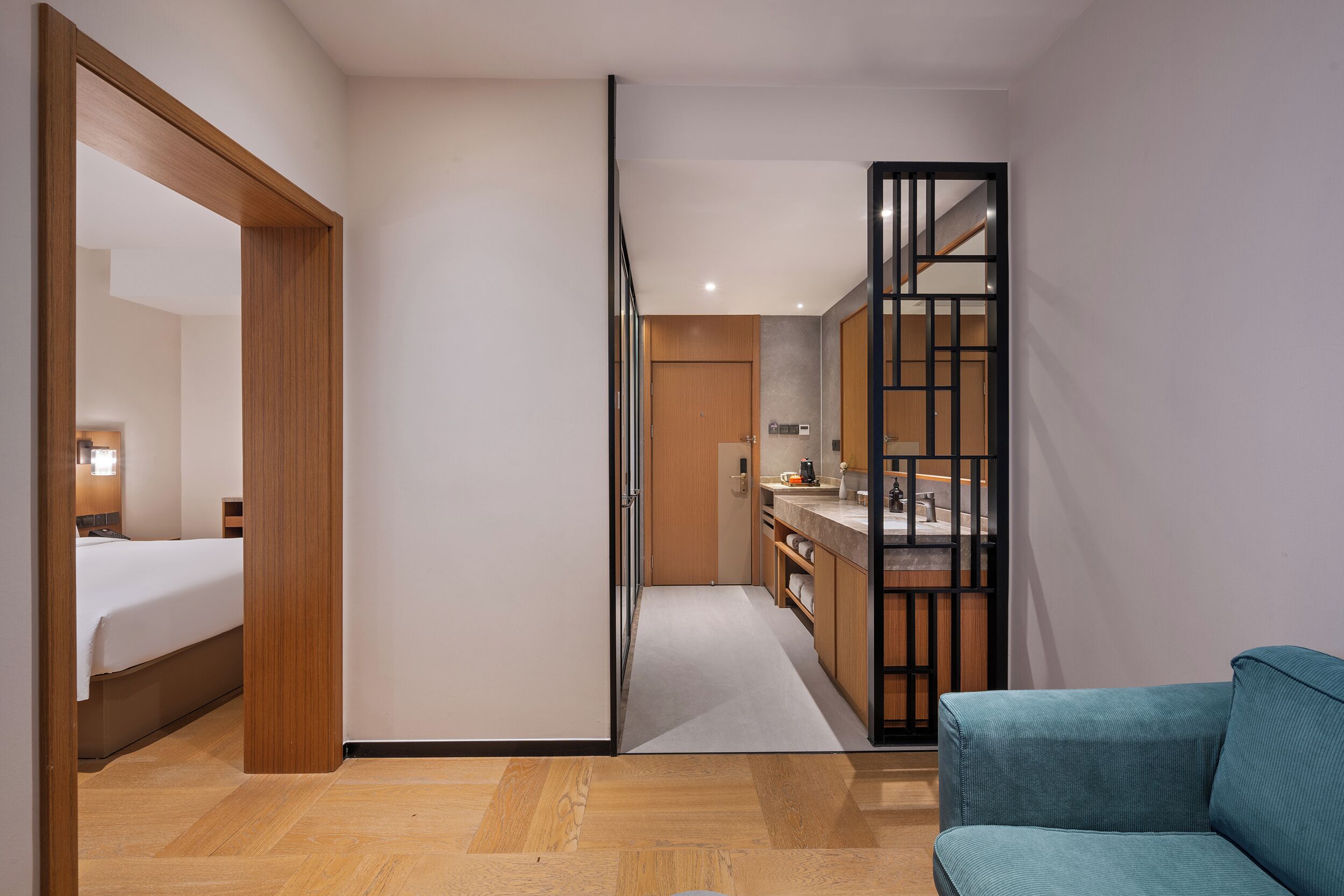 Una habitación de hotel con una cama, piso de madera, kitchenette y un sofá azul.