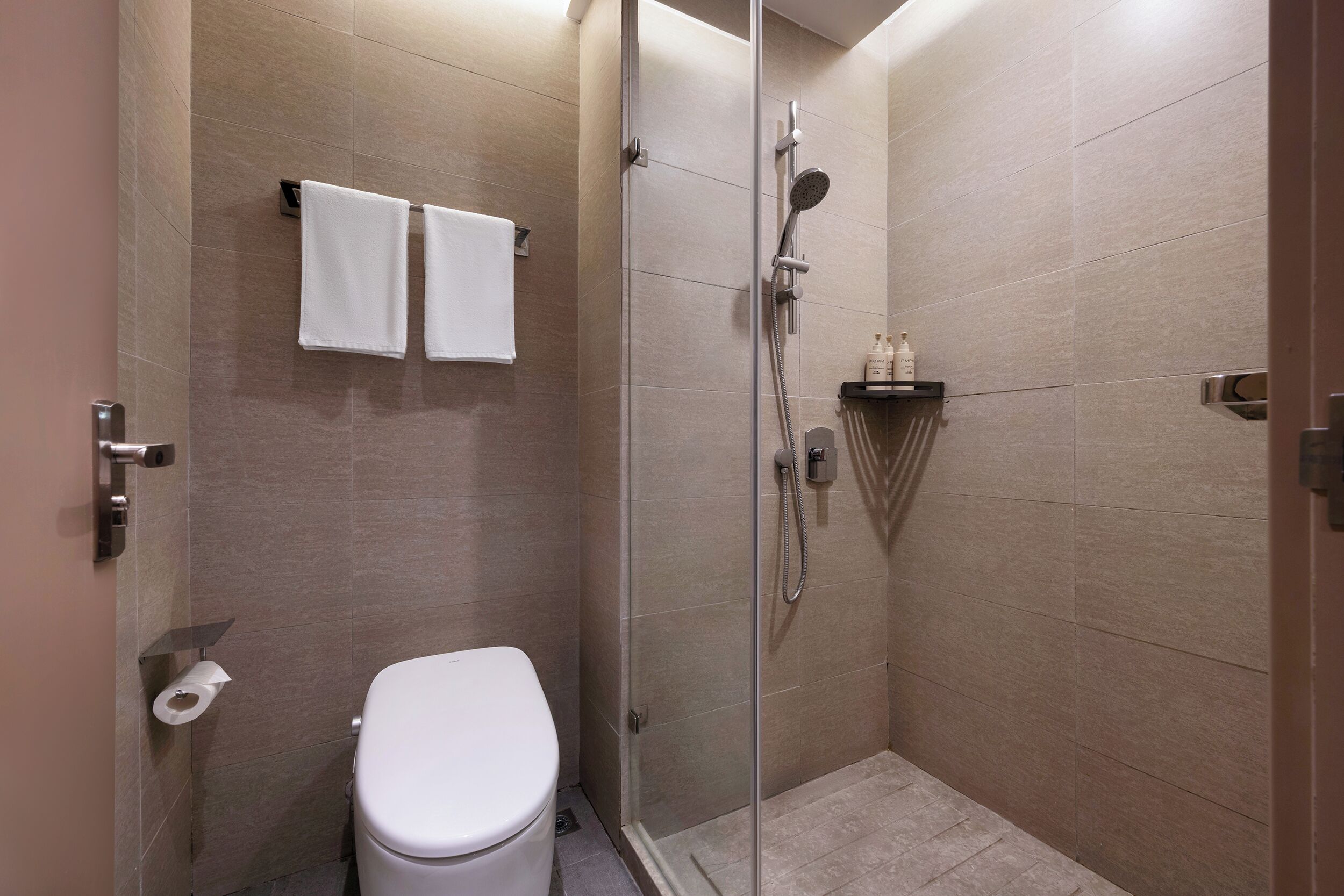 A modern bathroom with a glass-enclosed shower, a toilet, and a shelf with toiletries.