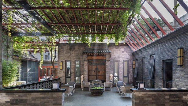 Ein Innenhof mit einer traditionellen Holztür, Ziegelmauern und einer Pergola mit Kletterpflanzen.