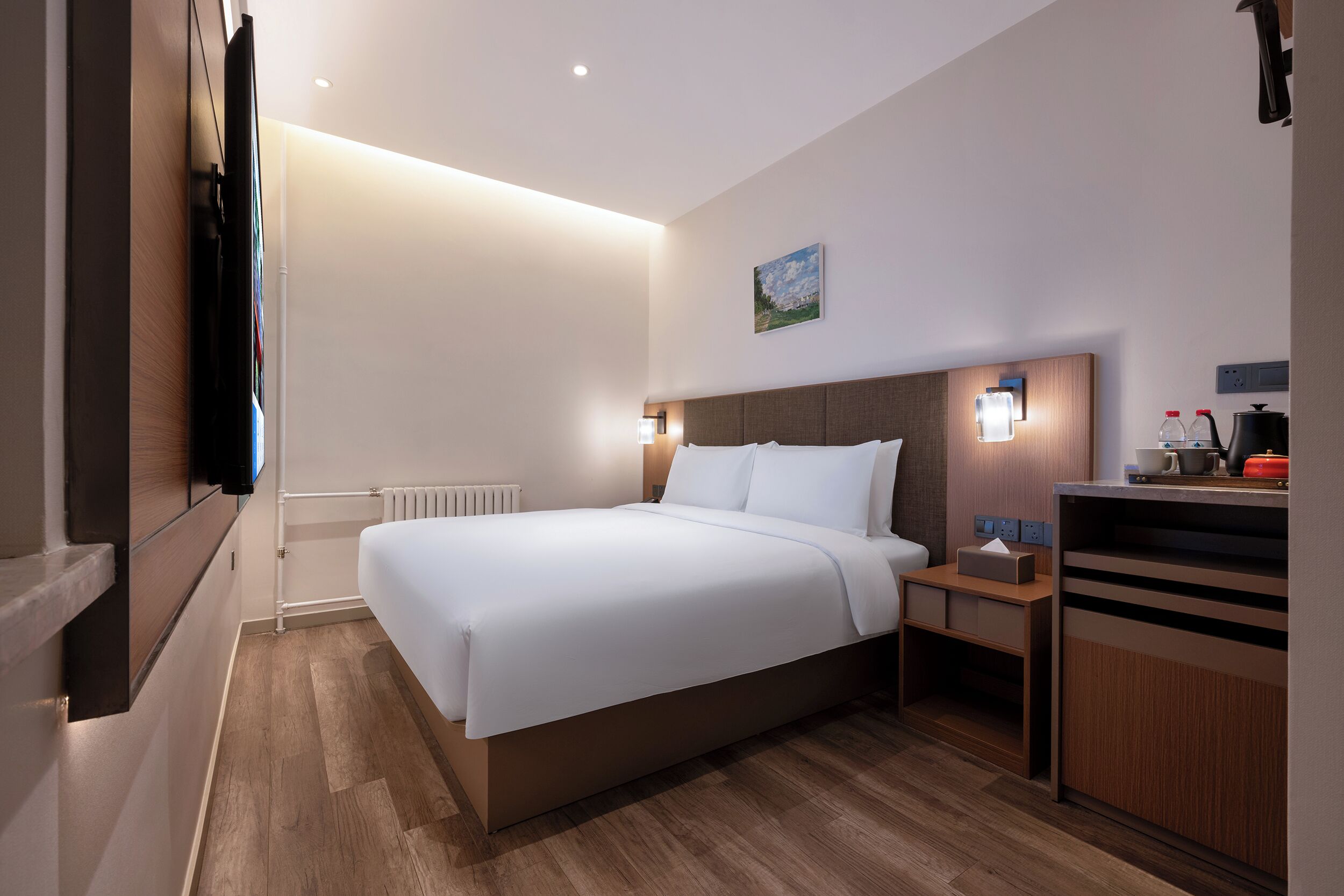 Ein modernes Hotelzimmer mit einem großen Bett, Nachttischen, einer kleinen Ablage und einem am Wand montierten Fernseher.