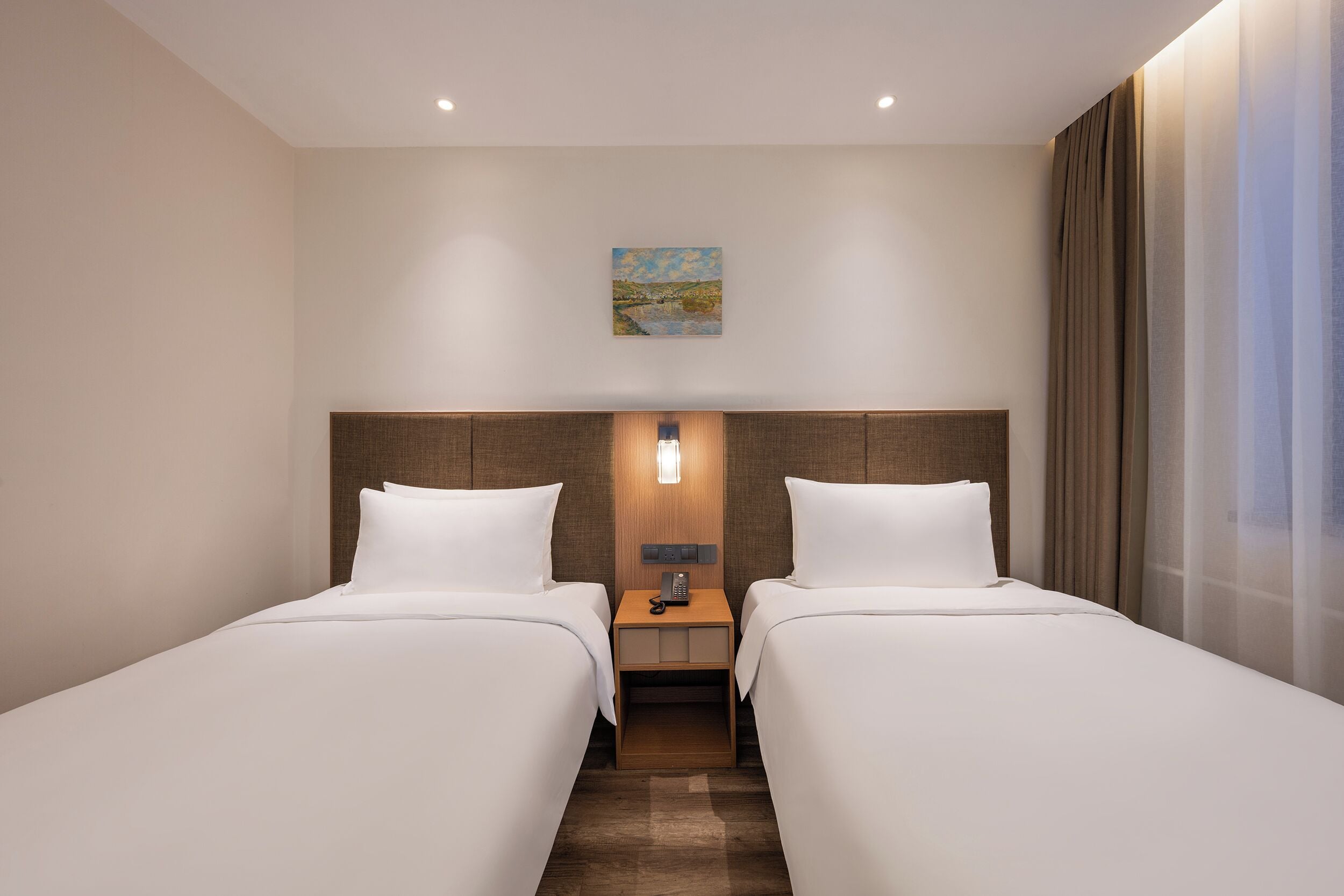 Ein Hotelzimmer mit zwei Betten, einem Nachttisch mit Telefon, einem Bild an der Wand und einem Fenster mit Vorhängen.
