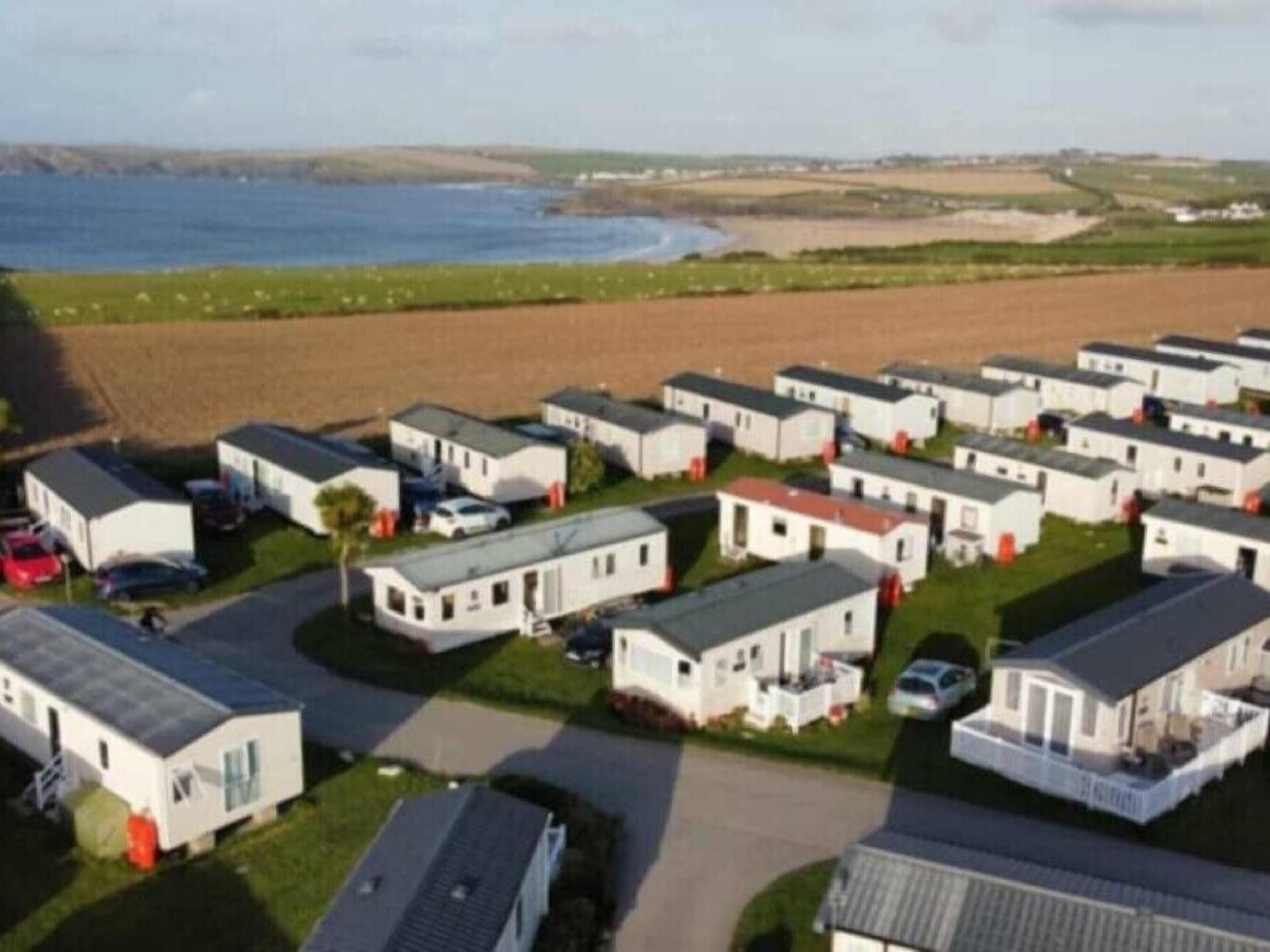 A caravan park with multiple white caravans, some with attached garages, and a beach in the background.