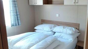 A single bed with white bedding, a wooden headboard, and a small bedside table. There are two cabinets above the bed, one with a black object on top.