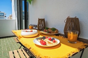 Ein Esstisch mit Frühstücksgebäck, ein Glas Orangensaft und ein Korbstuhl auf einem Balkon.