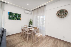Uma área de refeições com uma mesa posta para quatro pessoas, um sofá cinzento e uma pequena planta.