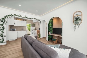 Ein modernes Wohnzimmer mit einer Küche, einem grauen Sofa und einem Fernseher.