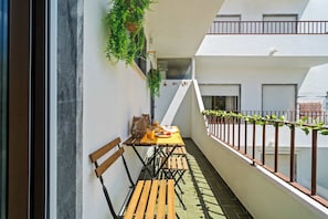 Varanda com mesa posta para dois, um banco de madeira e corrimão com plantas.