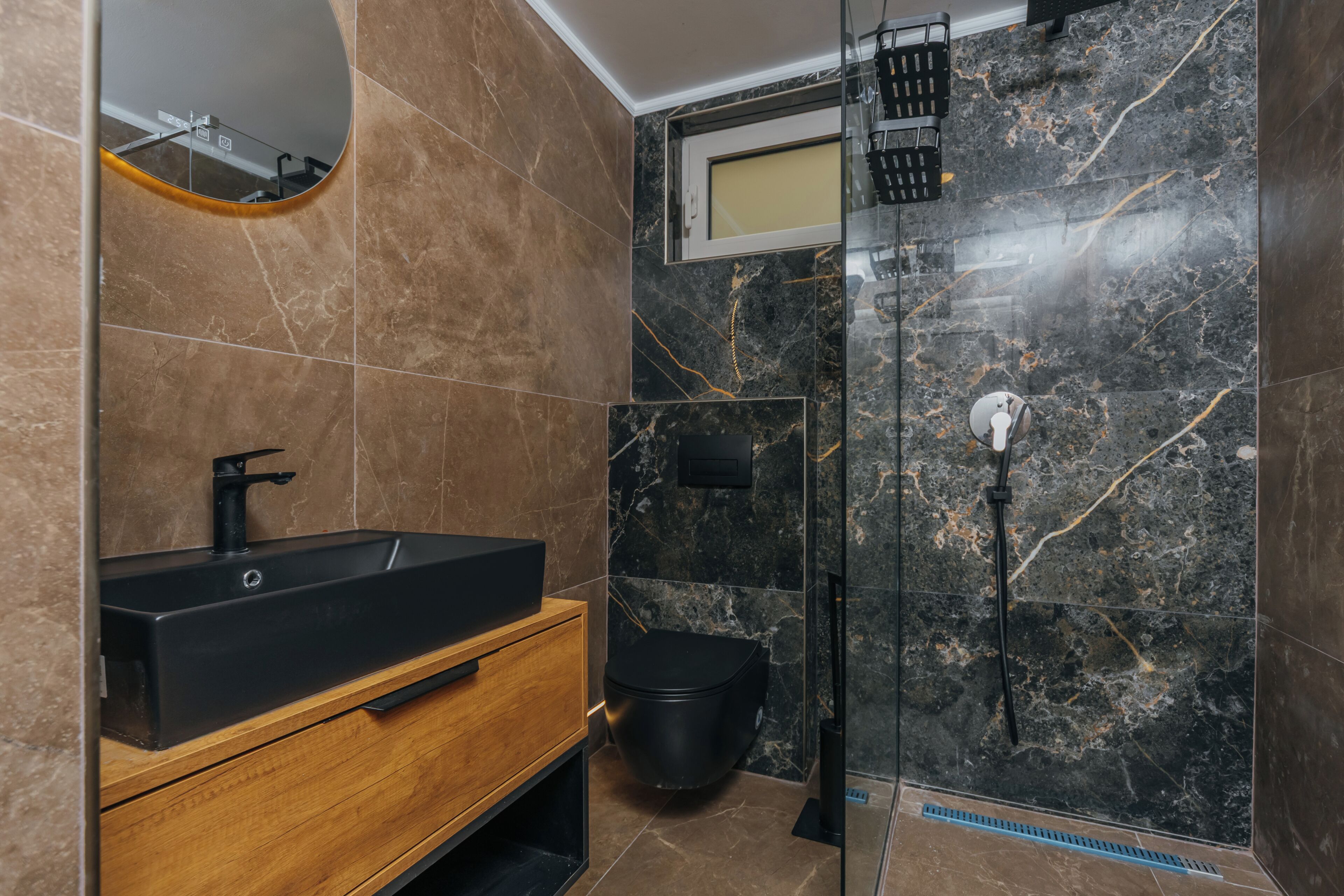 Une salle de bain avec un lavabo noir, un meuble-lavabo en bois, des toilettes et une cabine de douche en verre.
