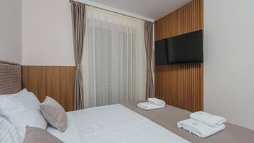 Una habitación de hotel con cama, almohadas, una televisión montada en la pared y una ventana con cortinas.