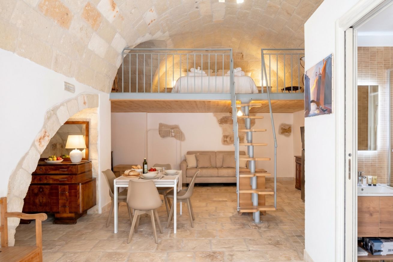 Une pièce chaleureuse avec un plafond en pierre, un lit superposé, un coin repas avec une table et des chaises, et un escalier.