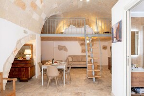 Una habitación acogedora con techo de piedra, una litera, un comedor con mesa y sillas, y una escalera.