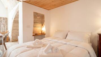 A bedroom with a wooden ceiling, a bed with white bedding, and a stone wall with a light fixture.