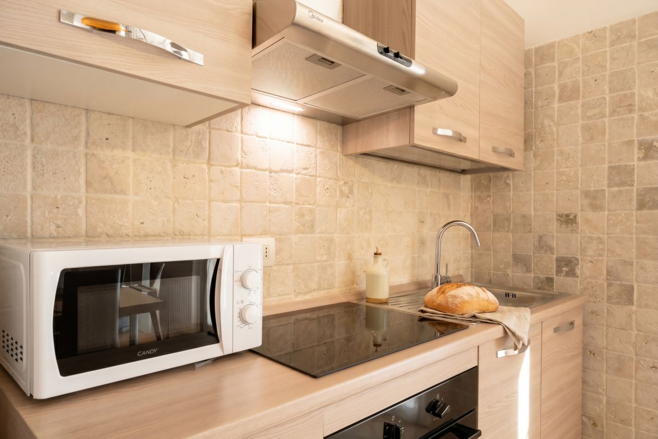 A kitchen with a microwave, a bread loaf, a milk bottle, and a sink.