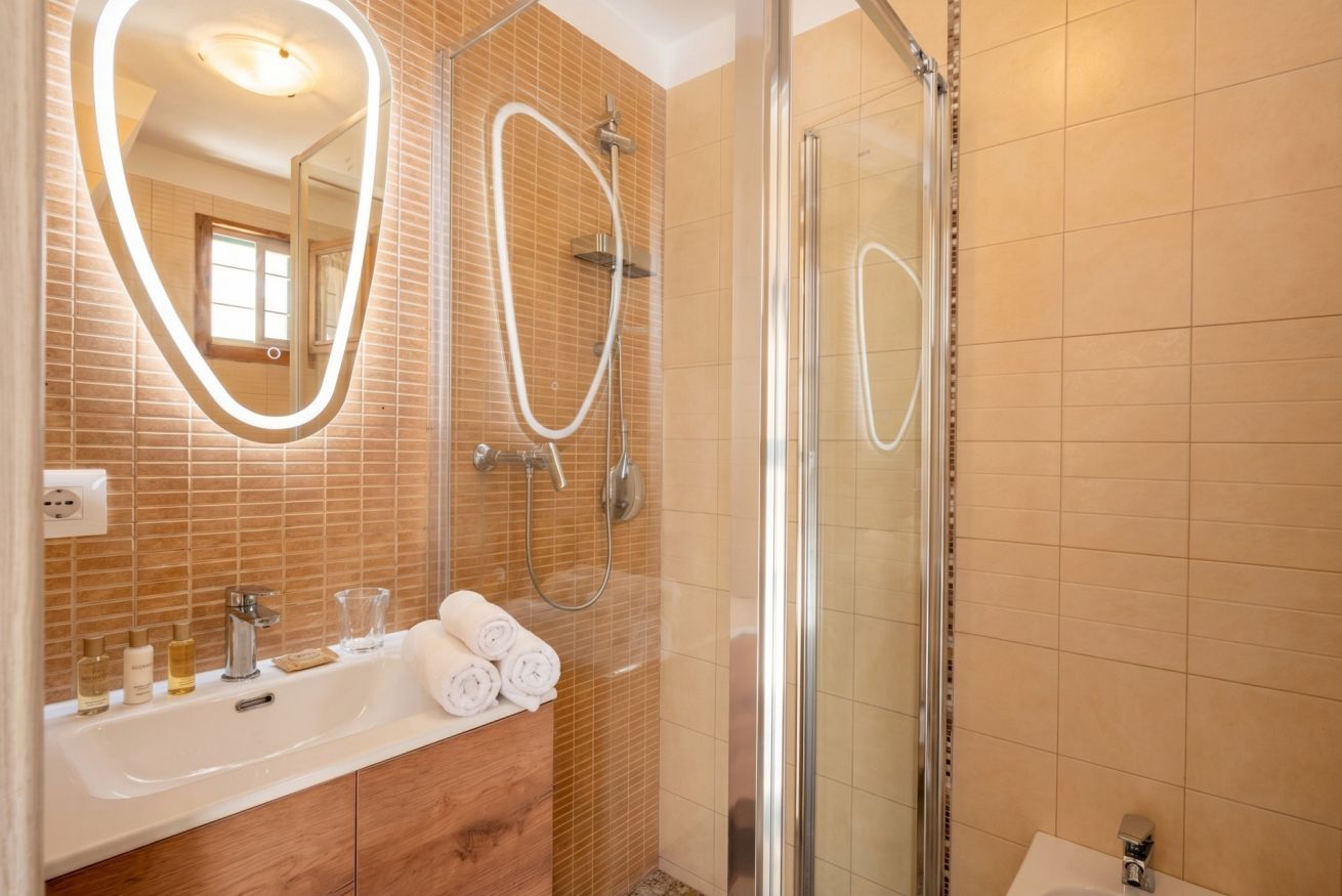 Un baño con cabina de ducha de vidrio, un espejo grande con iluminación, un lavabo con artículos de aseo personal y un tocador de madera.