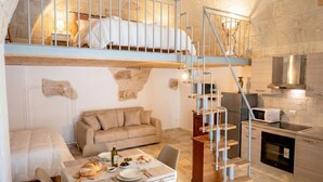 Une pièce compacte et rustique, comprenant un lit superposé, un coin repas, une kitchenette et un escalier.
