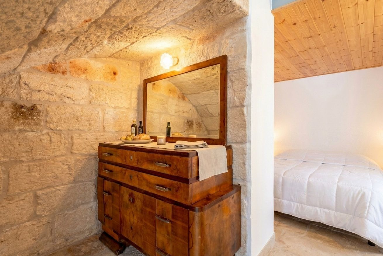 A bedroom with a stone wall, wooden dresser, and a bed.