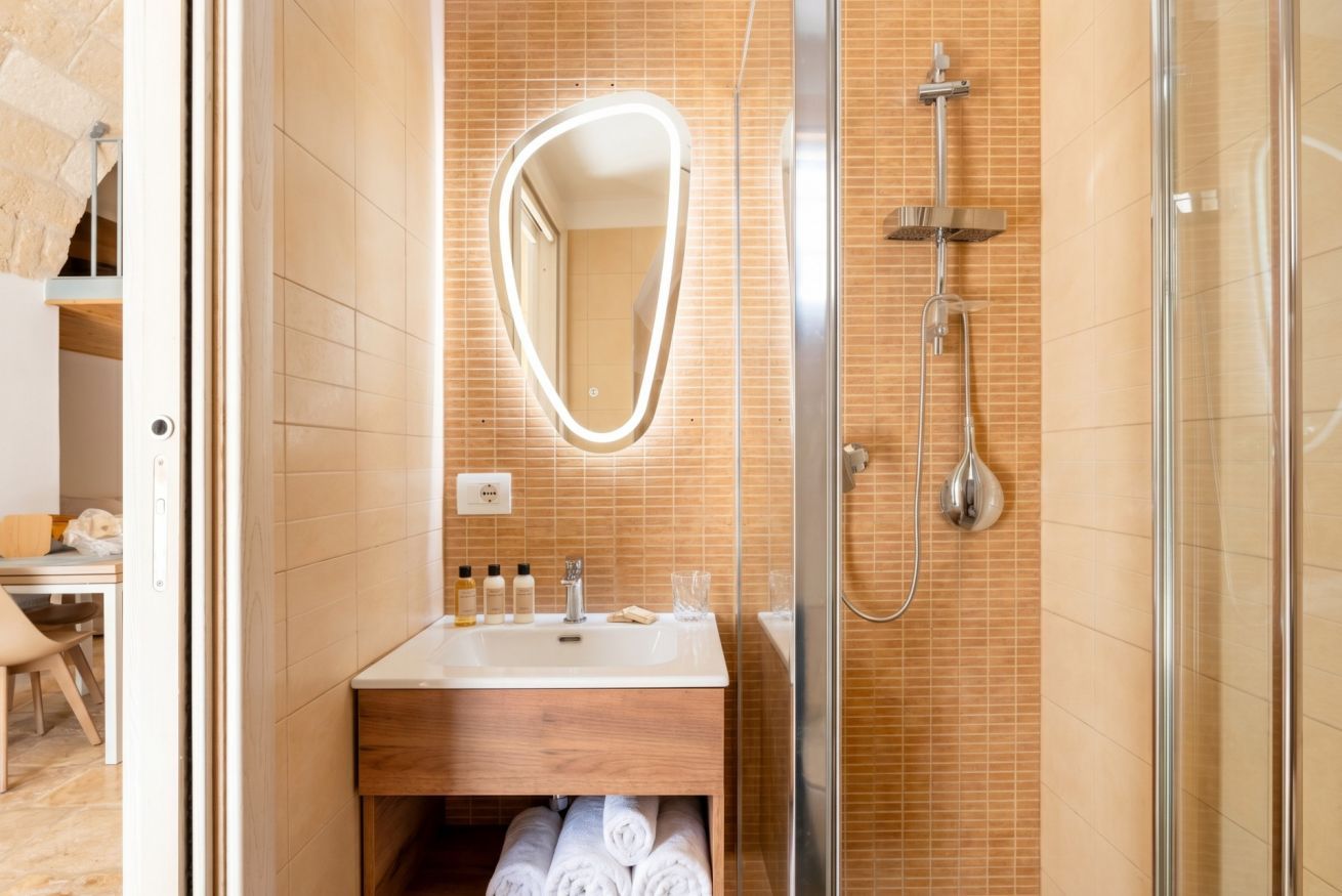 A bathroom with a shower, a sink with toiletries, and a mirror.