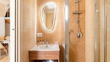 A bathroom with a shower, a sink with toiletries, and a mirror.