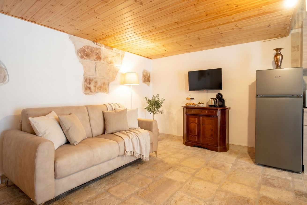 A room with a beige sofa, a wooden cabinet, a television, and a refrigerator.