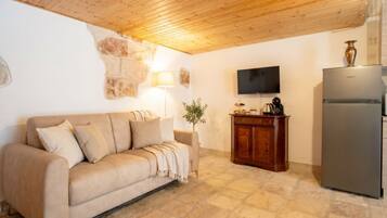 A room with a beige sofa, a wooden cabinet, a television, and a refrigerator.