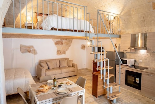 A compact, rustic room with a bunk bed, a dining area, a kitchenette, and a staircase.