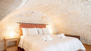 Une chambre avec un mur en pierre, un cadre de lit en bois, du linge de lit blanc et une lampe de chevet.