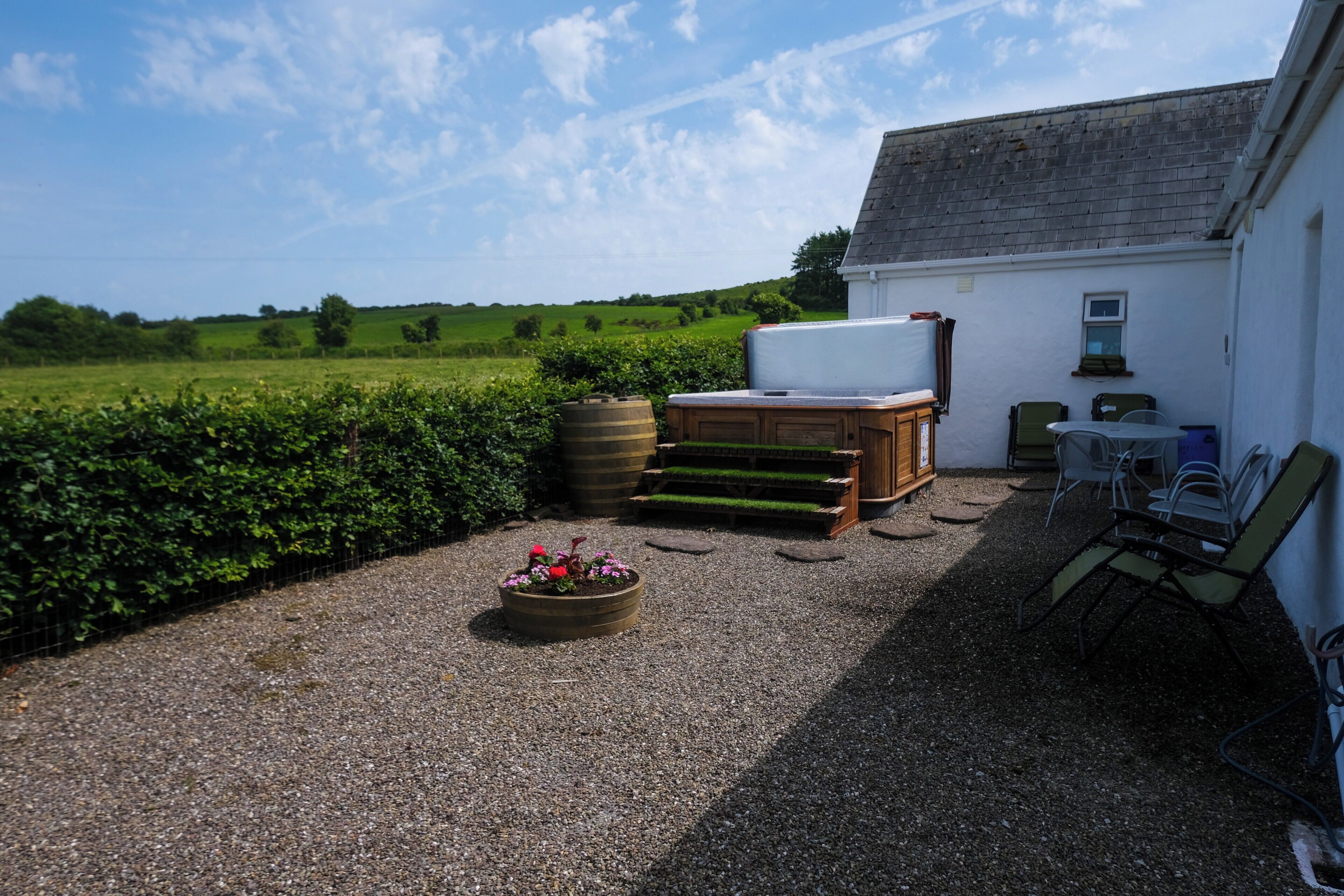 A gravel patio with a wooden bench, a white table, and a chair.