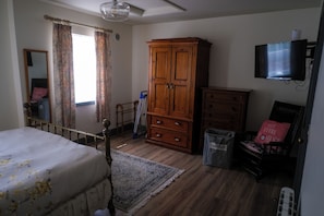 Une chambre à coucher comprenant un lit, une armoire en bois, une commode, un téléviseur et un miroir.