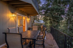 Eine überdachte Terrasse im Freien mit Tisch, Stühlen, einem Grill und Blick auf Bäume.
