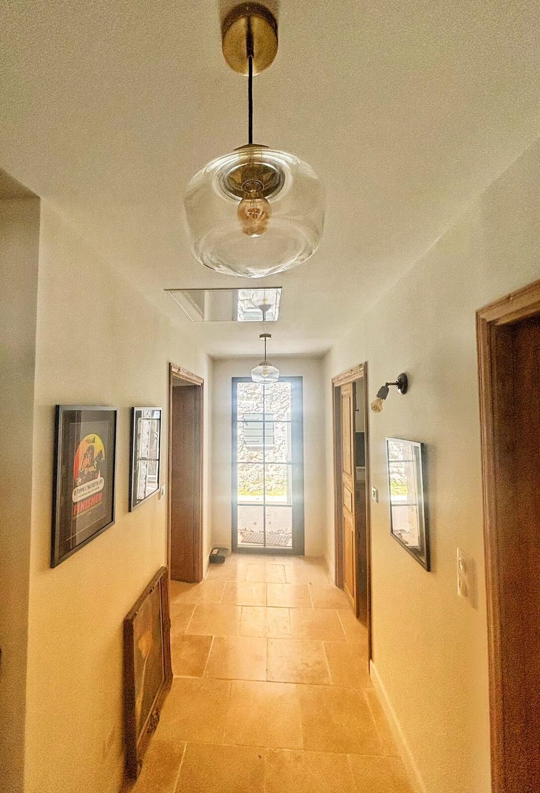 Un couloir avec un ventilateur de plafond, des tableaux encadrés accrochés aux murs et une porte au fond.