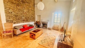 A living room with a stone wall, a fireplace, a sofa, a coffee table, and a guitar. - Stone house with swimming pool in the heart of the Corsican mountains. Near Corte (Corscia)