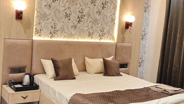 A modern bedroom with a central bed, bedside tables, an air conditioning unit, a ceiling fan, and a decorative wall panel. - ATITHI (Hisar)