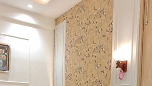 A room with a floral wallpaper, a framed picture on the wall, and a wall-mounted light fixture. - ATITHI (Hisar)