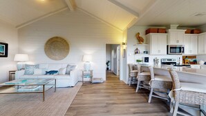 A spacious living area with a white sofa, a coffee table, and a dining area with wicker chairs. - Bolivar Bungalow: 1  BR, 1.5  BA House in Crystal Beach, Sleeps 5 (Crystal Beach)